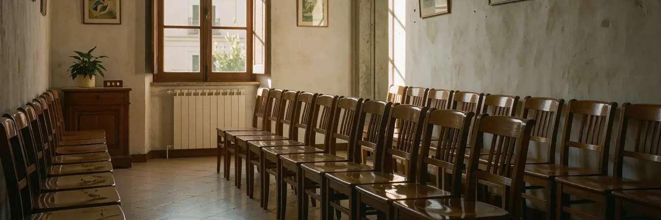 Sala de espera vacía con filas de sillas de madera y luz de tarde entrando por una ventana alta.